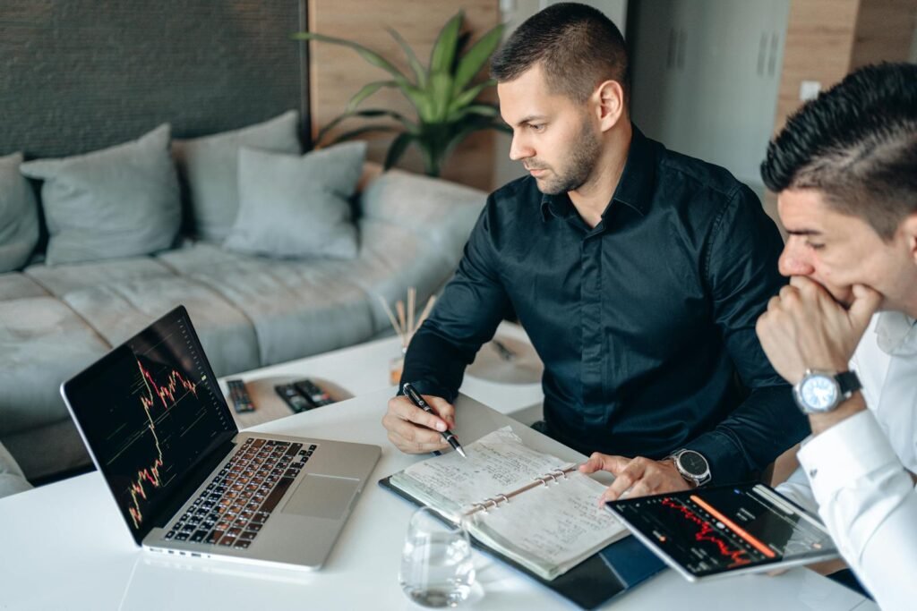 Two businessmen analyzing financial charts on laptop and tablet in office setting. How the rich think about money